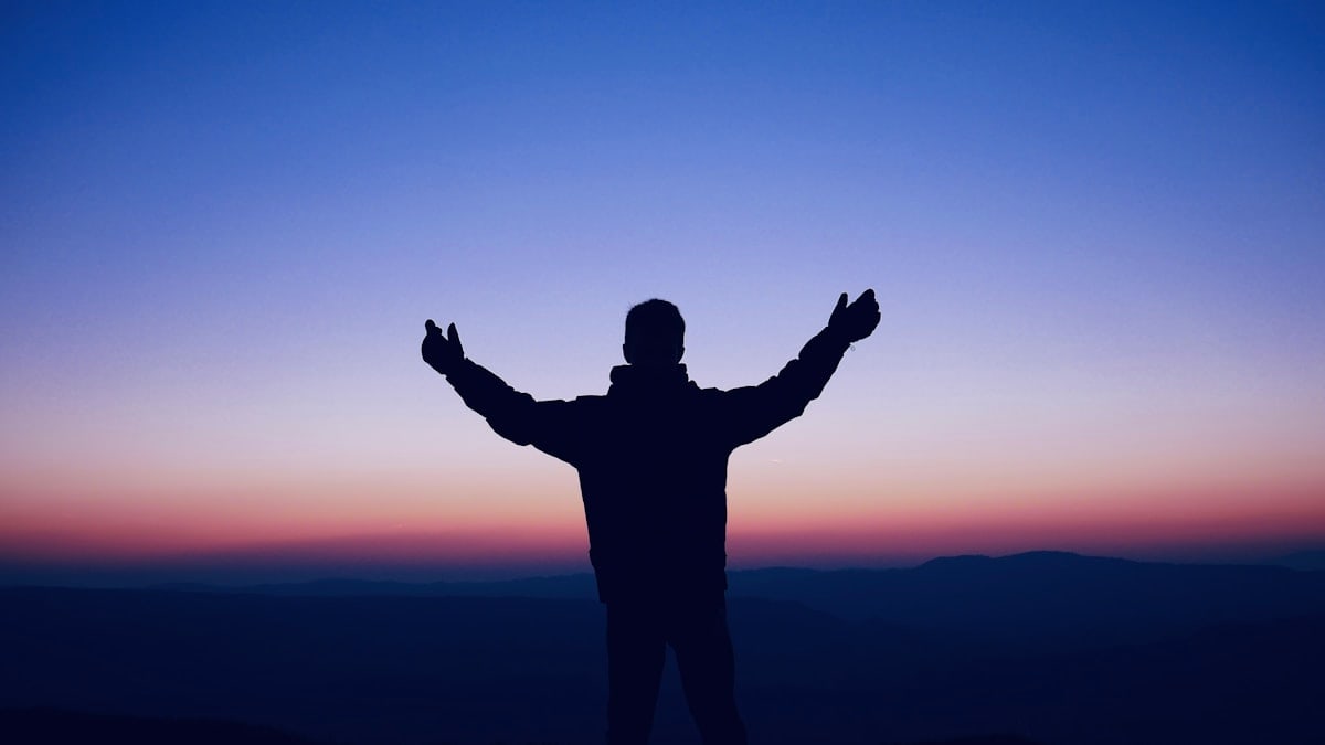 A man standing on top of a hill with his arms outstretched